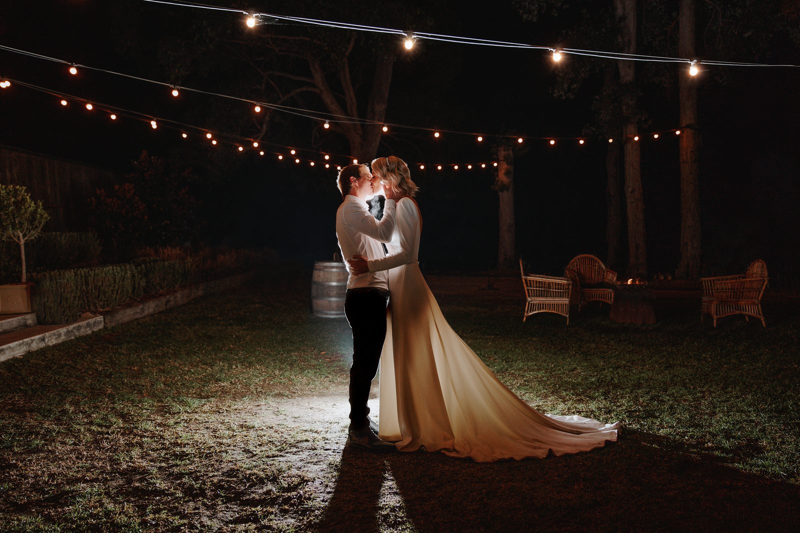 A couple kissing at night under festoon lights on the lawn