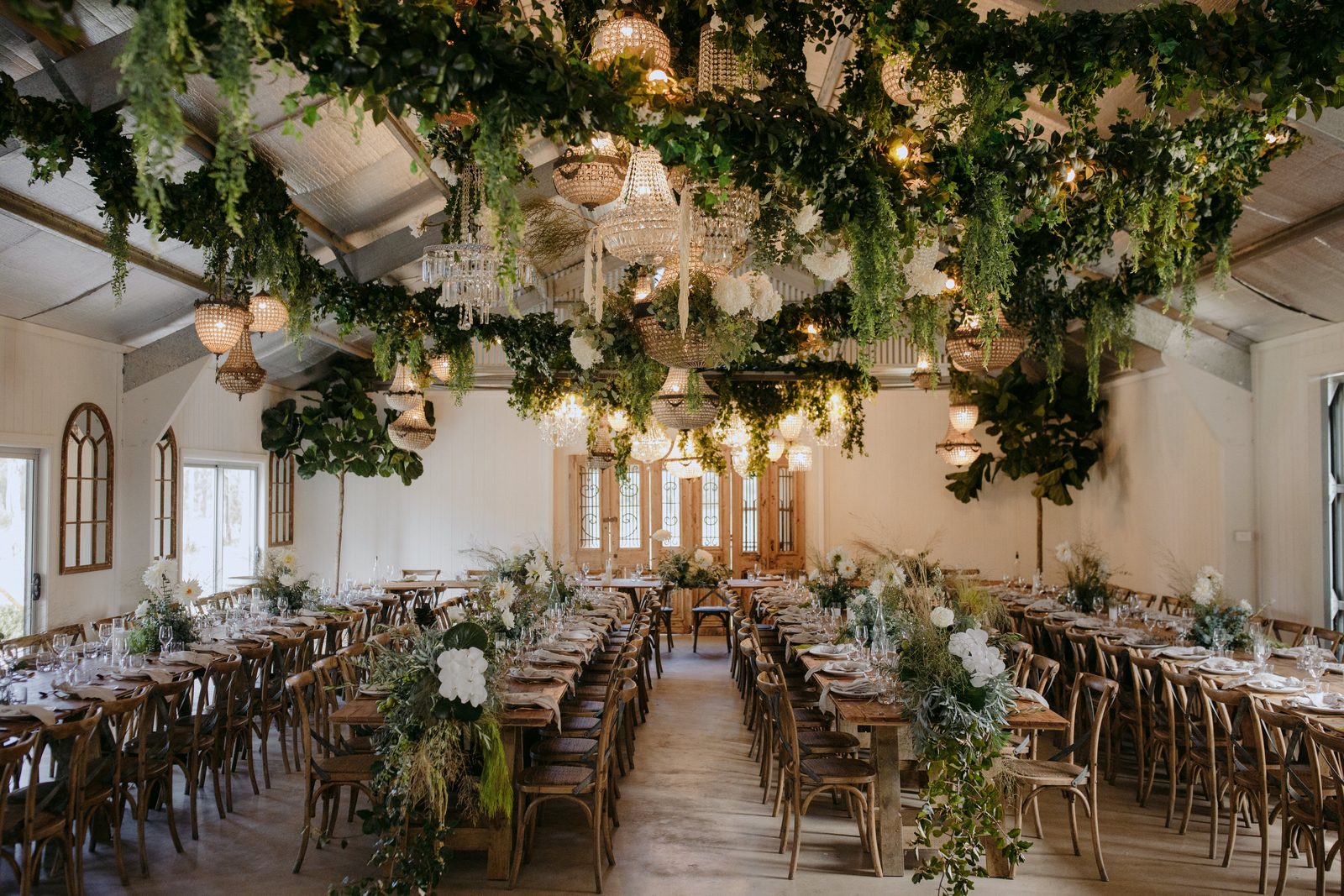 The Wedding Shed set with long timber tables under hanging greenery and chandeliers
